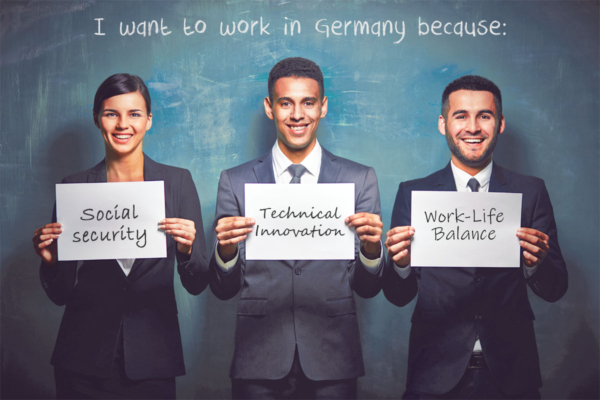Three foreign professionals show cards with their reasons for working in Germany. These reasons are: social security, technical innovation, work-life balance.
